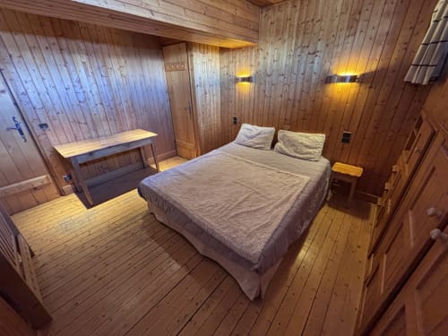 Rustic wooden bedroom with queen bed, desk, and warm lighting at Chez Francine apartment in Notre Dame de Bellecombe