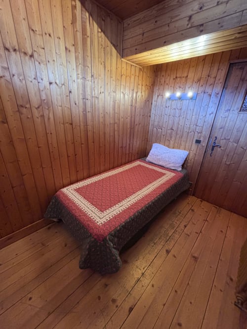 Cozy wooden bedroom with single bed, red bedding, and blue pillow at Chez Francine apartment in Notre Dame de Bellecombe