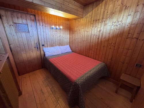 Cozy wooden bedroom with double bed, red bedding, and blue pillows at Chez Francine apartment in Notre Dame de Bellecombe