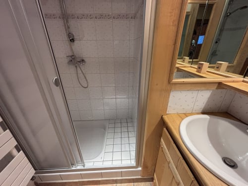 Bathroom with shower enclosure, white sink, wooden vanity, and mirror at Chez Francine apartment