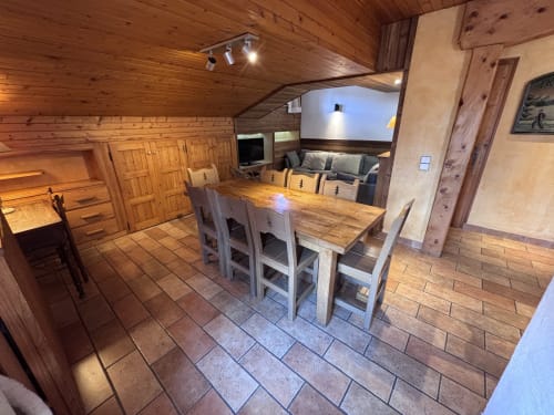 Spacious dining area in Chez Francine apartment with wooden table, chairs, and rustic wood-beamed ceiling in Notre Dame de