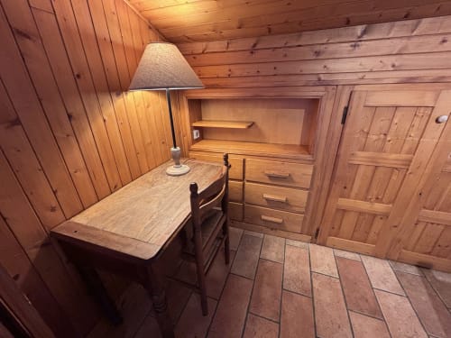 Cozy wood-paneled apartment bedroom at Chez Francine with desk, chair, lamp, dresser, and clay tile flooring