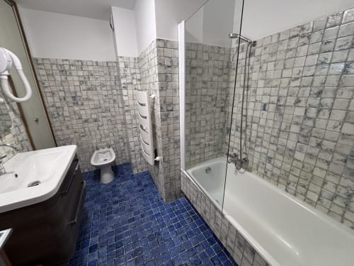 Modern bathroom with blue tile floor, white sink, toilet, and glass-enclosed shower/bathtub in Chez Francine apartment