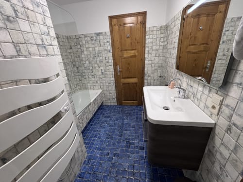 Modern bathroom in Chez Francine apartment with white sink, blue tile floor, wooden doors, and marble-tiled walls