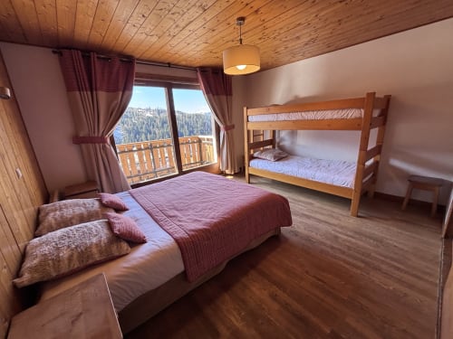 Spacious bedroom with queen bed, bunk beds, wooden ceiling, mountain views from balcony at Chez Francine, Notre Dame de