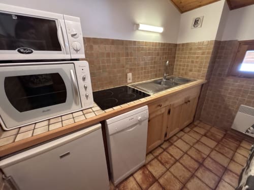 Compact kitchen in Chez Francine apartment with microwave, oven, cooktop, dishwasher, and sink with brown tile backsplash