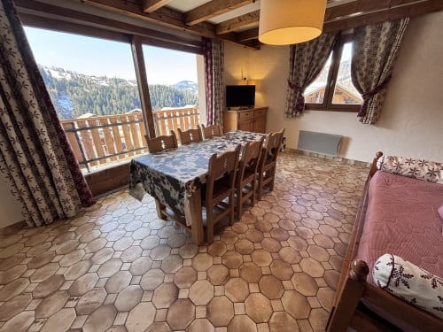 Spacious apartment dining and living area with mountain views, wooden beams, dining table, TV, and balcony at Chez Francine,