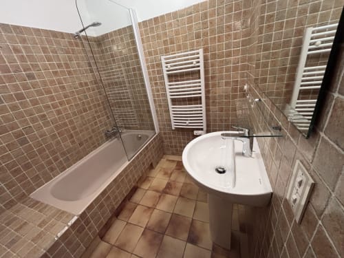 Modern bathroom with bathtub, white pedestal sink, heated towel rails and brown tile walls at Chez Francine, Notre Dame de