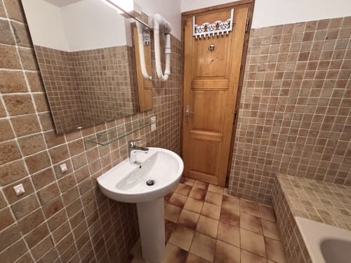 Modern bathroom at Chez Francine with white pedestal sink, brown tile walls, mirror, and wooden door in Notre Dame de