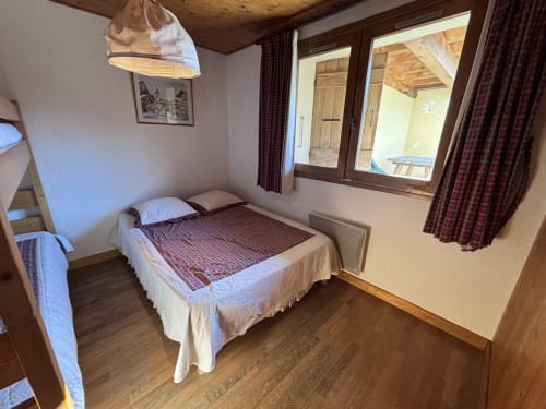 Cozy bedroom in Chez Francine apartment with double bed, wooden beams, burgundy curtains, and garden view in Notre Dame de