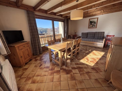 Bright alpine apartment living room with wooden beams, dining table, sofa, and mountain views from balcony at Chez Francine