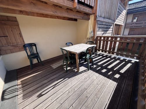 Sunny balcony with wooden deck, dining table, chairs, and alpine village view at Chez Francine, Notre Dame de Bellecombe