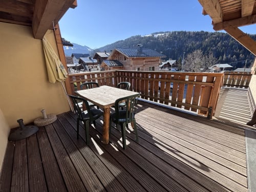 Spacious wooden balcony at Chez Francine in Notre Dame de Bellecombe with dining table, mountain views, and forest backdrop.