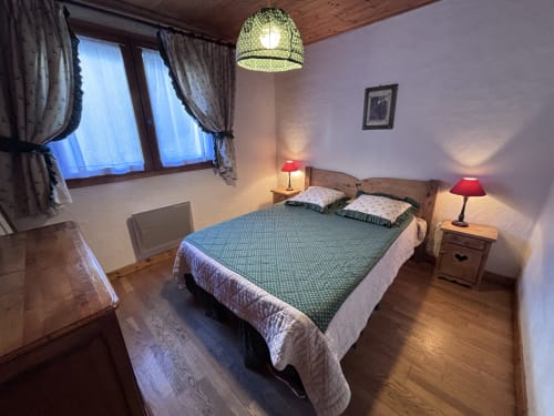 Cozy bedroom at Chez Francine apartment with double bed, red lamps, wooden furniture, and window with garden view in Notre