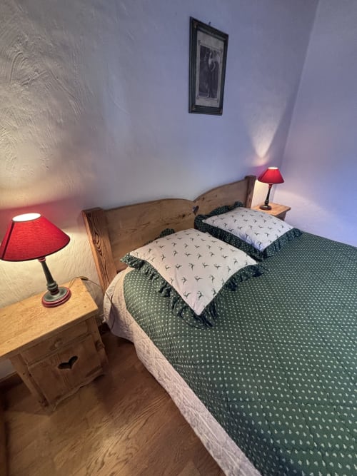 Cozy twin bedroom at Chez Francine with wooden beds, green patterned bedding, red lamps, and framed artwork in Notre Dame de