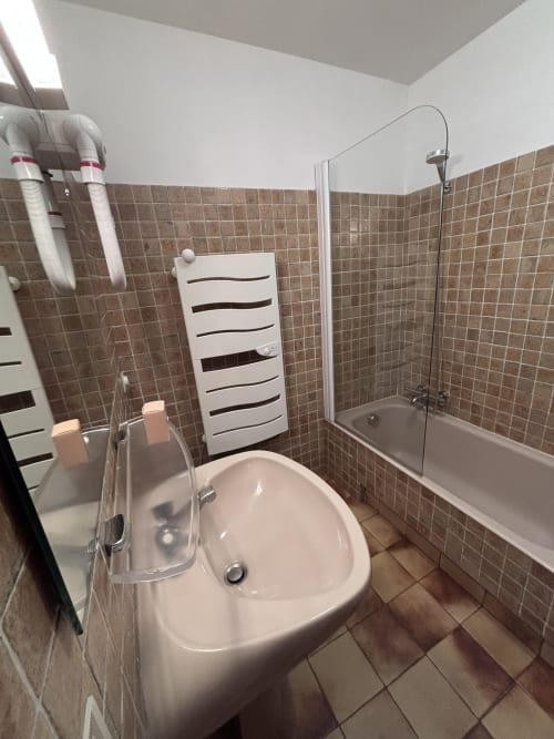 Modern bathroom with white sink, bathtub with shower screen, and heated towel rail at Chez Francine apartment, Notre Dame de