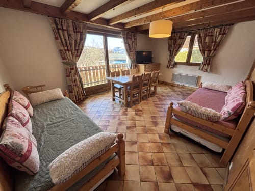 Spacious apartment bedroom at Chez Francine with two beds, dining table, balcony view, and rustic wooden beams in Notre Dame