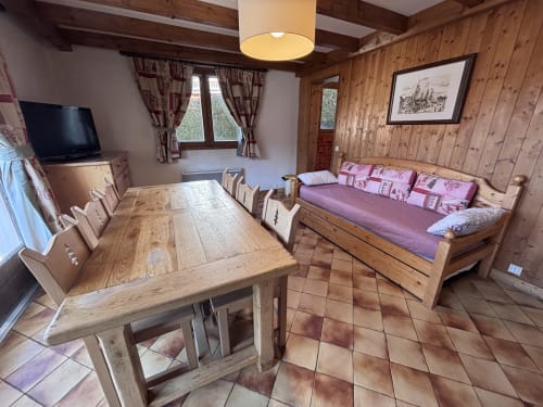 Cozy wooden apartment interior with dining table, purple sofa, TV, and mountain view window at Chez Francine, Notre Dame de