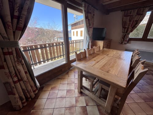 Dining room with wooden table, chairs, and balcony overlooking mountains at Chez Francine apartment in Notre Dame de
