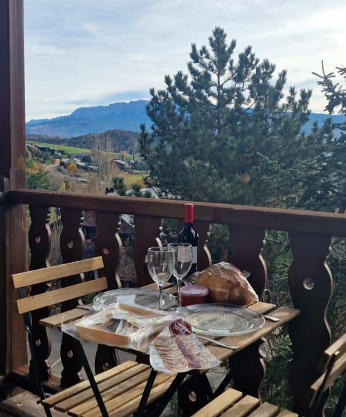 Comedor en la terraza de Mas D'En Roqueta con vistas a la montaña, vino, pan y charcutería frente al paisaje catalán
