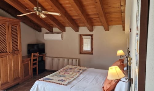 Amplia habitación del Hotel Mas D'En Roqueta con vigas de madera vista, cama doble, armario de madera y ventanal con balcón en España