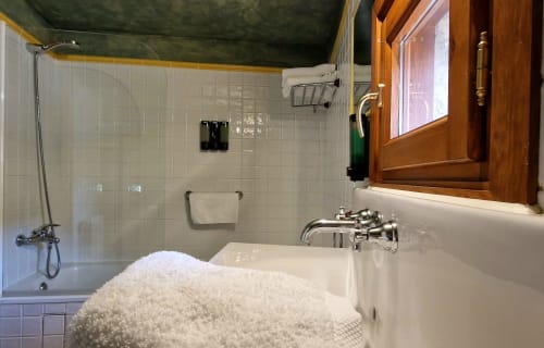 Baño de lujo en Hotel Mas D'En Roqueta con azulejos blancos, ducha de cristal, bañera, ventana de madera y toallas blancas suaves