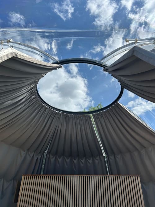 Vue intérieure de la chambre à dôme transparent de Bubble Jade avec lucarne circulaire encadrant le ciel bleu et les nuages