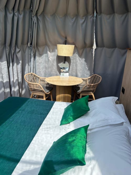 Chambre d'hôtel Bubble Jade avec coussins en velours vert sur le lit, chaises en rotin et table ronde en bois près de rideaux gris
