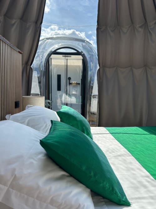 Chambre de la Bulle Émeraude à Bubble Jade avec oreillers verts, lit et vue sur la structure en forme de bulle avec patio