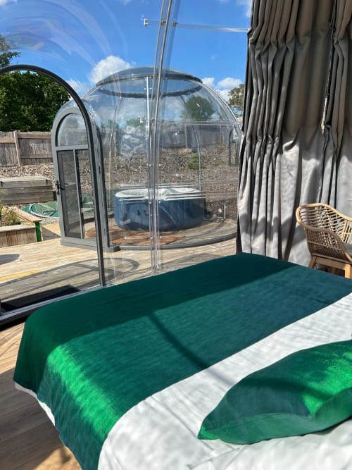 Literie verte sur terrasse en bois avec jacuzzi privé sous dôme transparent et vue sur le jardin à l'hôtel Bubble Jade, Bazouges la Pérouse