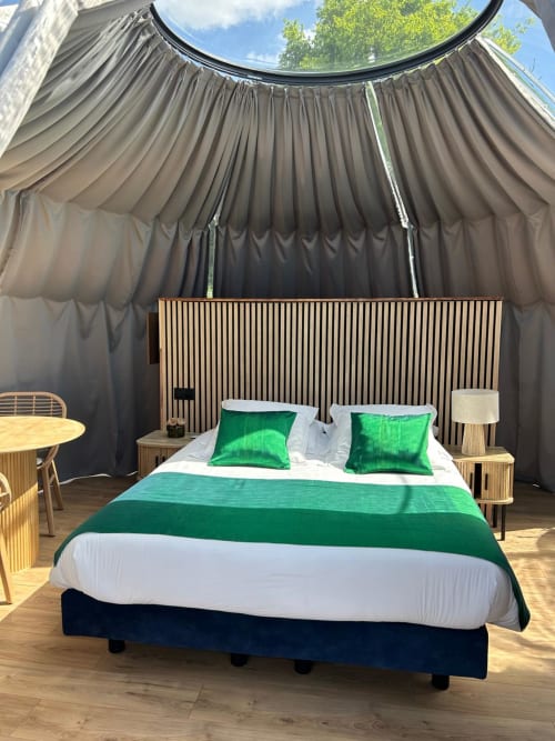 Chambre Bulle Émeraude à l'hôtel Bubble Jade avec accents verts, tête de lit en bois et rideaux courbes sombres donnant sur le jardin