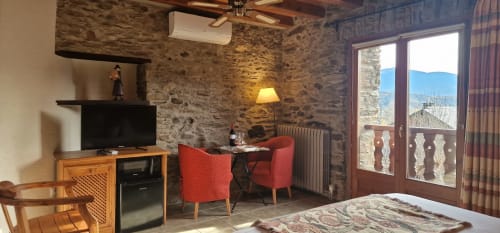 Habitación doble de lujo en Hotel Mas D'En Roqueta con muros de piedra, equipamiento moderno y vistas a montañas desde balcón