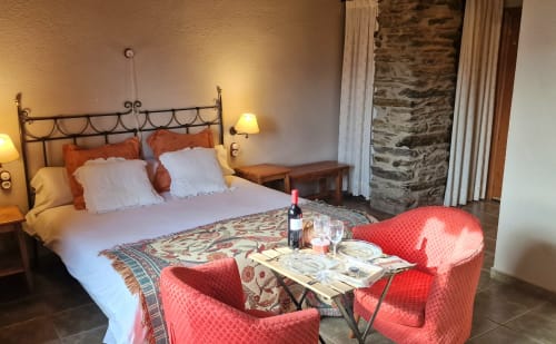 Lujosa habitación doble en Hotel Mas D'En Roqueta con cama de hierro forjado, sillones rojos, servicio de vinos y arquitectura de piedra