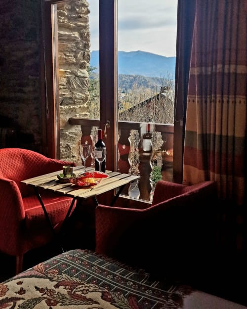 Habitación de lujo en Hotel Mas D'En Roqueta con butacas rojas, vistas a la montaña, muros de piedra y servicio de vinos