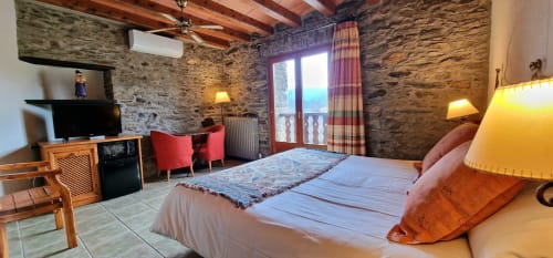 Habitación doble superior del Hotel Mas D'En Roqueta con paredes de piedra, vigas de madera, cama, TV, sillas rojas y acceso a terraza