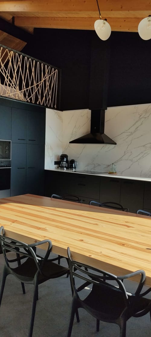 Cocina y comedor moderno con mesa de madera, sillas negras, pared de mármol y luces colgantes en Mas d'en Roqueta