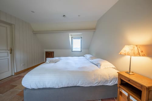 Chambre lumineuse sous les combles de la villa La Girelle à Honfleur avec lit queen-size, lucarne, table de nuit en bois et lampe chaleureuse