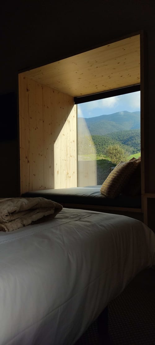 Dormitorio moderno de madera con ventanal panorámico que enmarca vistas de montaña y bosque en la casita Hotel Mas D'En Roqueta