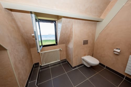 Salle de bain moderne avec vue sur la mer à la villa La Girelle, Honfleur. Carrelage noir, murs beige, sanitaires blancs.