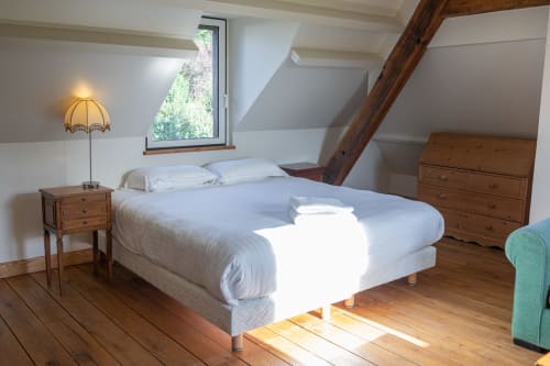 Chambre lumineuse sous les toits de la villa La Girelle à Honfleur avec literie blanche, poutres apparentes et vue sur mer