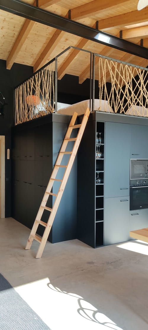Interior moderno tipo loft con vigas de madera, barandillas negras, detalles de cuerda y escalera de madera hacia el entresuelo