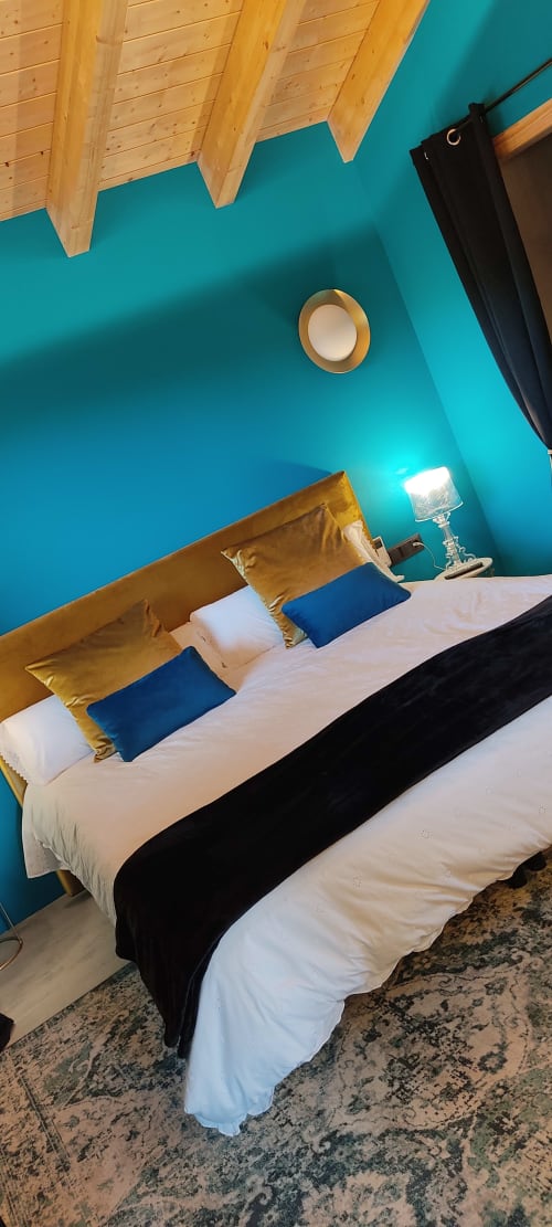 Habitación turquesa luminosa con vigas de madera, cama blanca y cojines dorados y azules en Casa Mas d'en Roqueta