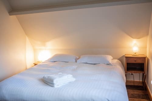 Chambre douillette de la villa La Girelle à Honfleur avec literie blanche, table de nuit en bois et éclairage chaleureux
