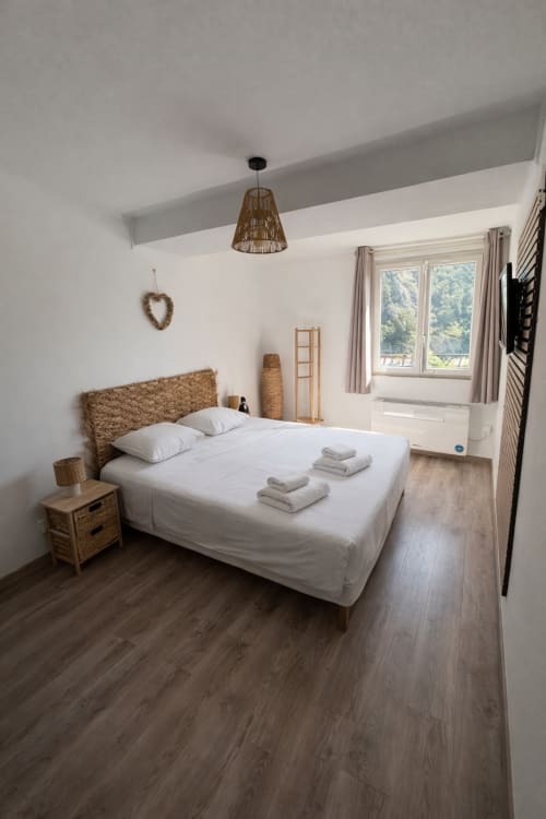 Chambre lumineuse et contemporaine à l'hôtel Le Clos Androne à Sisteron avec tête de lit en tissu tressé, draps blancs et vue sur les montagnes