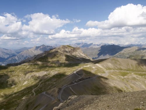 Paysage alpin près de Jausiers avec route sinueuse, pentes verdoyantes et sommets lointains