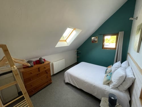 Chambre mansardée aux Prairies du Val d'Amboise, Noizay, avec lit blanc, mur d'accent bleu canard, lucarne et commode en bois