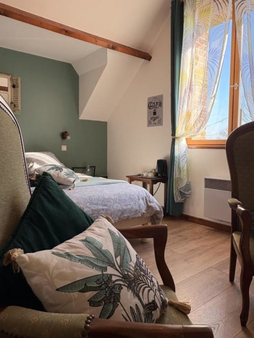 Chambre douillette à la Ferme de la Forterie avec mur d'accent vert, poutre en bois apparent et rideaux botaniques à Verlinghem