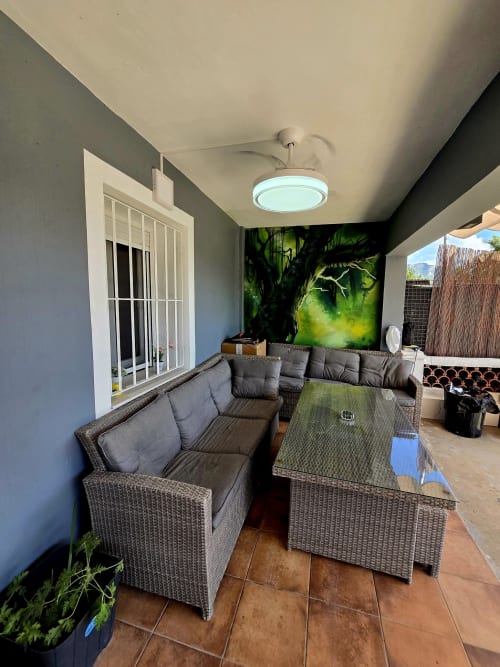 Terraza cubierta con asientos de mimbre, cojines grises, mesa de café y arte tropical en Casa Rural El Bressol