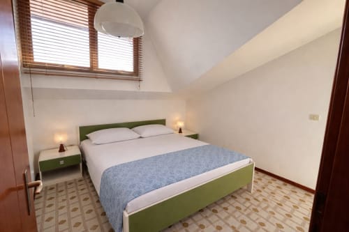 Bright bedroom with green bed frame, white bedding, skylight windows, and patterned floor at Anthea hotel in Lignano