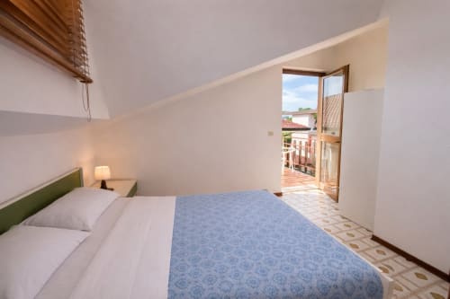 Bright bedroom with blue bedspread, green headboard, and open glass door to balcony at Anthea Hotel, Lignano Sabbiadoro